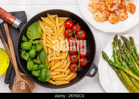 Eine lebendige Darstellung der italienischen Flagge mit Pasta, Basilikum und Tomaten, wunderschön präsentiert in einer Pfanne. Flach verlegt Stockfoto