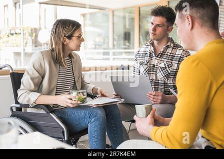 Junge Geschäftsleute, die sich im Büro treffen und eine Frau im Rollstuhl sitzen Stockfoto