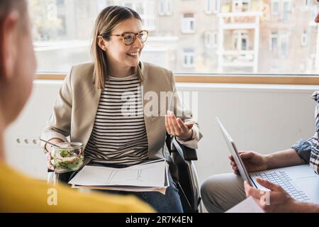 Lächelnde junge Geschäftsfrau im Rollstuhl, die ein Meeting im Büro hat Stockfoto