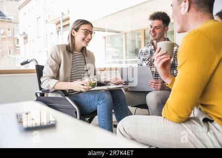 Junge Geschäftsleute, die sich im Büro treffen und eine Frau im Rollstuhl sitzen Stockfoto
