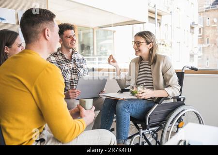 Junge Geschäftsleute, die sich im Büro treffen und eine Frau im Rollstuhl sitzen Stockfoto