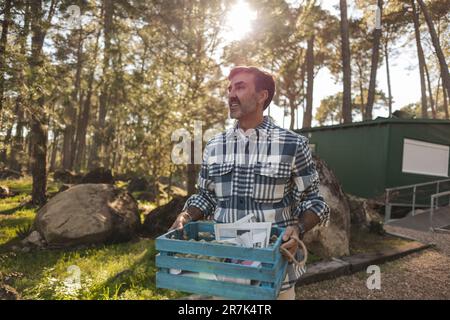 Reifer Mann, der Kiste mit getrenntem Abfall im Garten trägt Stockfoto