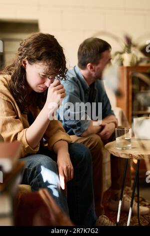 Vertikales Bild einer gestressten Frau, die auf dem Sofa sitzt und weint, während sie Psychologin mit Ehemann besucht Stockfoto