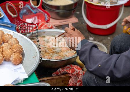 Nahaufnahme der Hand über einer Bratpfanne eines Mannes mit Stäbchen, der auf dem Bac-Ha-Sonntagsmarkt in Vietnam Doughy-Fischbällchen zubereitet Stockfoto
