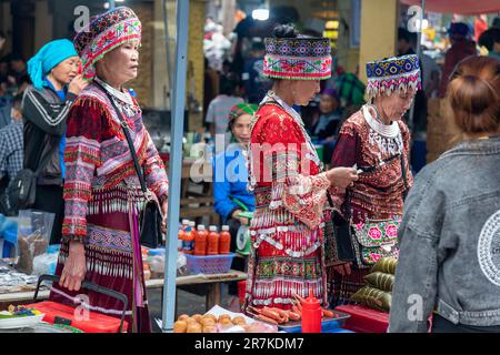 BAC Ha, Vietnam-April 2023; Nahaufnahme von drei Frauen von Flower Hmong und Giay in farbenfroher Kleidung, die Gemüse auf dem Sonntagsmarkt kaufen Stockfoto