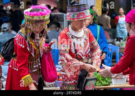 BAC Ha, Vietnam-April 2023; Nahaufnahme von zwei Frauen von Flower Hmong und Giay in farbenfroher Kleidung, die Gemüse auf dem Sonntagsmarkt kaufen Stockfoto