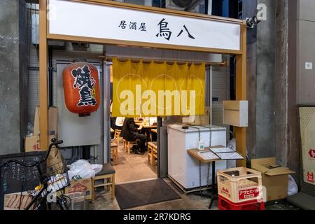 Tokio, Japan - April 2023; abendlicher Blick auf die Fassade eines kleinen Restaurants im Viertel Yurakucho unter Steinbögen (Gado-shita) erhöhter Bahnschienen Stockfoto