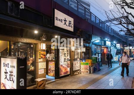 Tokio, Japan - April 2023; Abendblick entlang kleiner Restaurants im Viertel Yurakucho unter Steinbögen (Gado-shita) erhöhter Bahnschienen Stockfoto