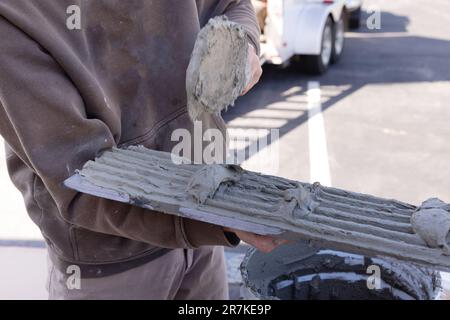 Mann, der feuchten Zementklebstoff aufträgt, bevor er Fliesen aufträgt, mit dem Arbeiter, der Glättwerkzeuge verwendet Stockfoto