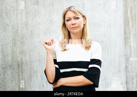 Außenporträt einer Frau mittleren Alters, die sich an eine graue Wand lehnt Stockfoto