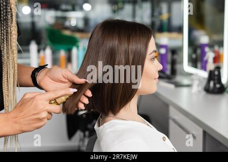 Schönheitssalon, professioneller Stylist mit Zöpfen, die das Haar der Frau mit Öl bestreichen, Haarstyling, Haarbehandlung, Frisur, Verlängerung, Salon-Kunde Stockfoto