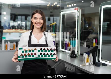 Friseursalon, glückliche Schönheitsarbeiterin in der Schürze, die Haarfarbe im Schönheitssalon zeigt, Haarverlängerung, Friseurin, Haarfarbe, Friseurjob, Schönheitssalon Stockfoto