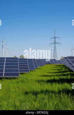 Solarenergieanlage mit Stromleitungen und Windturbinen im Hintergrund, wie man sie in Deutschland sieht Stockfoto