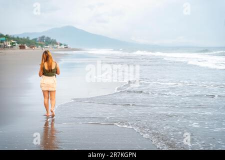 Halten Sie ihr Handy für Selfies, an einem Strand in der Nähe von Manila in der Dämmerung, schlendern Sie ziellos durch die warmen Küstengewässer, entlang des sanften Sandes, haben Sie Spaß, tanzen Sie herum Stockfoto