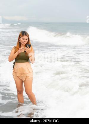 Halten Sie ihr Handy für Selfies, an einem Strand in der Nähe von Manila in der Dämmerung, schlendern Sie ziellos durch die warmen Küstengewässer, entlang des sanften Sandes, haben Sie Spaß, tanzen Sie herum Stockfoto