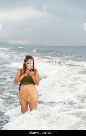 Halten Sie ihr Handy für Selfies, an einem Strand in der Nähe von Manila in der Dämmerung, schlendern Sie ziellos durch die warmen Küstengewässer, entlang des sanften Sandes, haben Sie Spaß, tanzen Sie herum Stockfoto