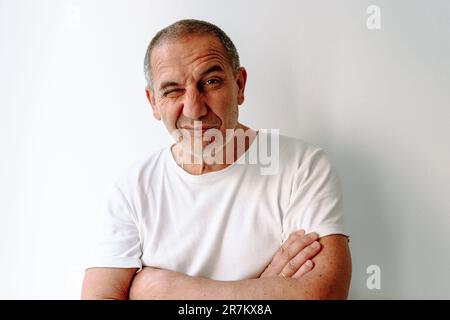 Ein Mann mittleren Alters in einem weißen T-Shirt mit Grimace im Gesicht auf weißem Hintergrund Stockfoto