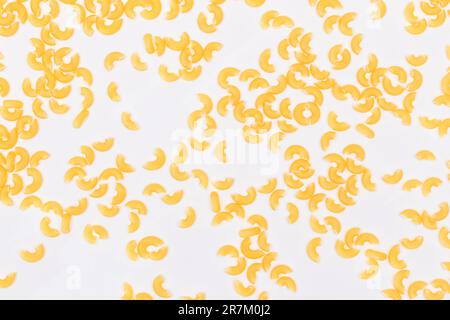 Verstreute ungekochte Chifferi Rigati Pasta auf weißem Hintergrund. Fett und ungesunde Lebensmittel. Klassische Trockene Makkaroni-Textur. Italienische Kultur und Küche. Rohe Pasta Stockfoto