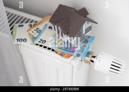 Neuer Thermostat mit Euro-Bargeld auf einer Heizkörperheizung zu Hause. Teure Heizkosten symbolisches Image. Stockfoto