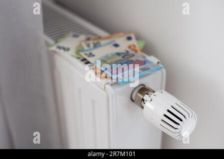 Neuer Thermostat mit Euro-Bargeld auf einer Heizkörperheizung zu Hause. Teure Heizkosten symbolisches Image. Stockfoto