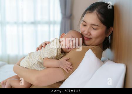 Die asiatische Mutter umarmte ihren jungen Sohn, damit sie zu Hause im Schlafzimmer gut schlafen konnte, sie repräsentiert Liebe und Familie Stockfoto