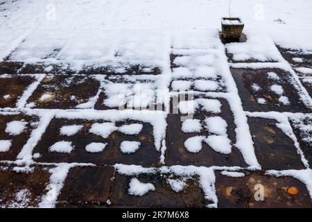 Ungewöhnliche Fleckmuster mit Domino-Effekt, wenn der Schnee im Winter auf einer Terrasse in einem Garten in Surrey, Südostengland, schmilzt Stockfoto