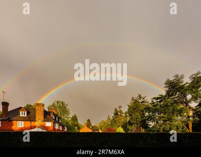 Ein komplett bunter Doppelregenbogen über dem Garten und den Bäumen eines großen Hauses in Woking, Surrey, Südostengland im Frühling Stockfoto