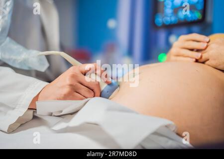 Im Krankenhaus, Nahaufnahme des Arztes tut Ultraschall Sonogramm Verfahren zu einer schwangeren Frau. Beweglicher Schwinger für Geburtshelfer am Bauch von Stockfoto