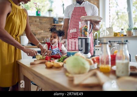 Die afroamerikanische Familie kommt zusammen, um in ihrer Küche eine Mahlzeit zuzubereiten. Das Bild zeigt eine Mutter, einen Vater und eine Tochter, die zusammenarbeiten, Su Stockfoto