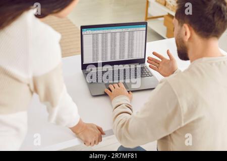 Zwei Geschäftsleute, die sich zurücklehnen und an einem Laptop mit Tischen im Büro arbeiten. Stockfoto