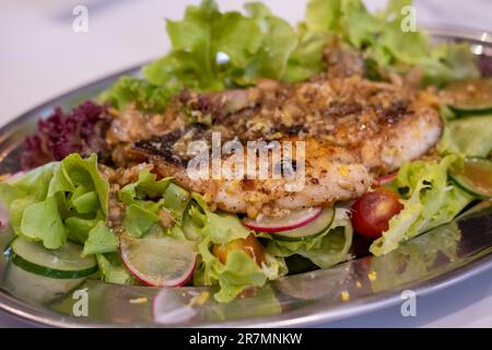 Gegrillter Fischsalat mit Gemüse und Tomaten, serviert auf einem Teller Stockfoto