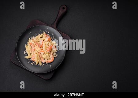 Köstliche frische penna-Pasta mit Garnelen, Sauce, Käse, Salz und Gewürzen auf dunklem Betonhintergrund Stockfoto