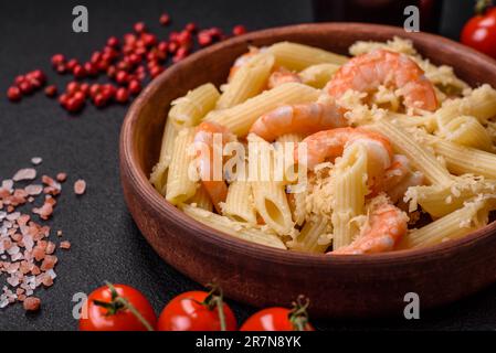 Köstliche frische penna-Pasta mit Garnelen, Sauce, Käse, Salz und Gewürzen auf dunklem Betonhintergrund Stockfoto