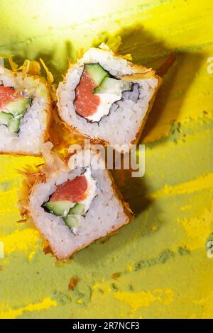 Blick von oben auf japanische Brötchen mit Fisch, Gurke und Käse auf gelbem Hintergrund Stockfoto