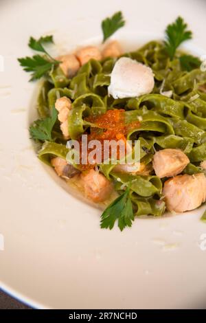 Nahaufnahme von grüner Pasta mit Lachs und rotem Kaviar und Grün auf einem weißen Teller Stockfoto