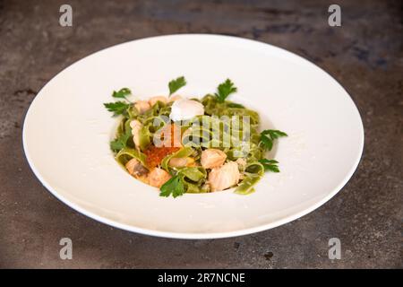 Grüne Pasta mit Lachs und rotem Kaviar und Grün auf einem weißen Teller Stockfoto