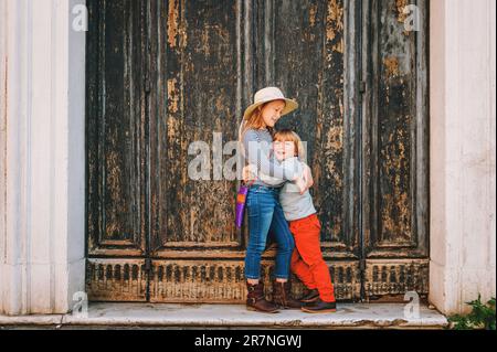 Außenporträt von süßen kleinen Jungen und Mädchen, stilvolle Kinder, die sich gegen alte grüne Türen posieren. Mode für Kleinkinder Stockfoto