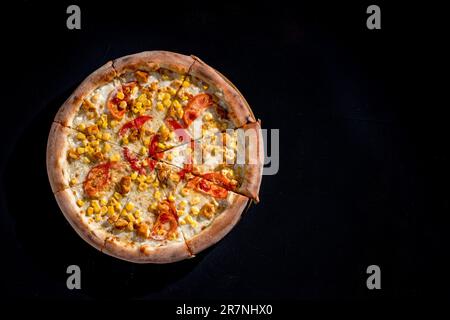 Pizza für Kinder auf Sahnebasis mit Hühnerfilet, Tomaten, Mais und Mozzarella-Käse auf schwarzem Hintergrund. Stockfoto