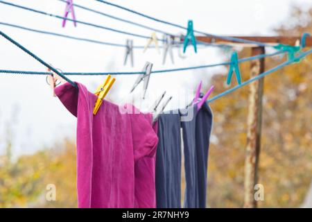 An der Wäscheleine hängt ein Wäschekorb. Ein Seil mit sauberer Bettwäsche und Kleidung draußen am Tag der Wäsche. Vor dem Hintergrund der grünen Natur Stockfoto