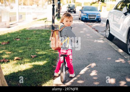 Außenporträt eines süßen kleinen Mädchens, das Fahrrad fährt, einen Rucksack trägt Stockfoto