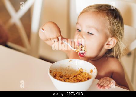 Ein liebenswertes Mädchen mit gutem Appetit isst Pasta mit Tomatensoße Stockfoto