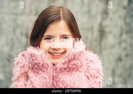 Nahaufnahme eines hübschen Mädchens mit blauen Augen, in einem rosa Mantel aus Kunstpelz, mit Händen am Kinn Stockfoto