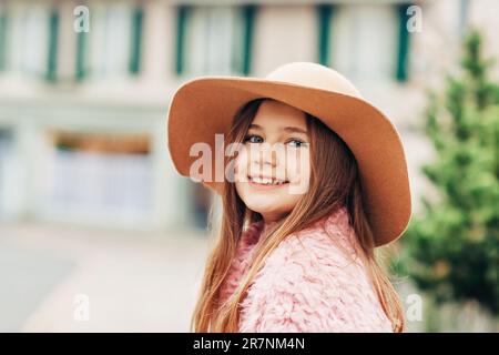 Außenporträt eines hübschen jungen Mädchens mit braunem Hut und pinkfarbenem Mantel, Straßenmode für Kinder Stockfoto