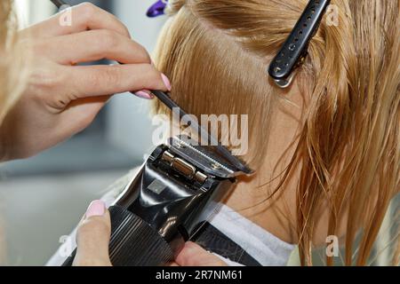 Ein professioneller Friseur verschönert das Haar einer Frau, letzte Akzente mit elektrischem Rasierer Stockfoto