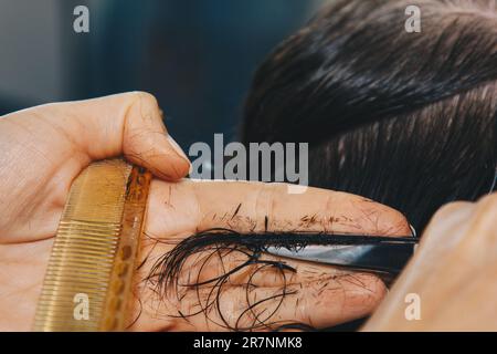 Die Nahaufnahme eines Friseurs schneidet das nassbraune Haar eines Kunden in einem Salon. Friseur schneidet eine Frau. Seitenansicht einer Hand, die mit einer Schere Haare schneidet Stockfoto