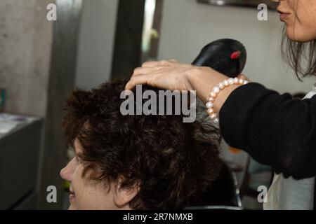 Nahaufnahme von Friseurhänden, die Menschenhaare mit Geräten trocknen. Eine Frau mit einem Kamm Stockfoto