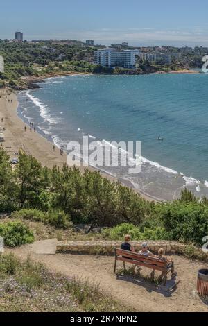 Zwei Frauen und ein Mann sitzen auf einer Bank am aussichtspunkt platja Llarga (langer Strand) auf dem Küstenpfad (Cami de Ronda), einer Route von Salou nach Llosa. Stockfoto