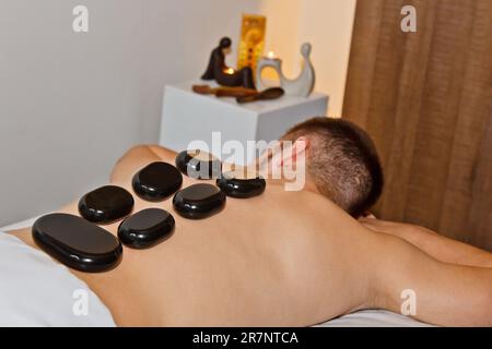 Wellnesskonzept. Attraktiver junger Mann, der sich unter dem stimulierenden Effekt einer traditionellen Hot-Stone-Massage in einem luxuriösen Spa und Wellnesscenter entspannen kann. Aufn Stockfoto