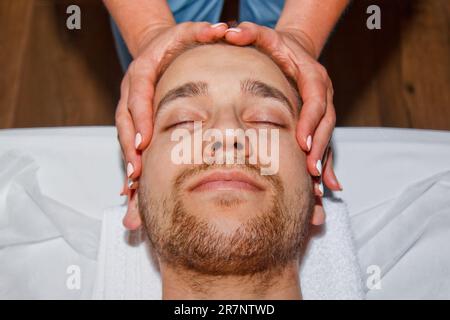 Wellnesskonzept. Ein professioneller Masseur gibt einem Mann eine Thai-Gesichtsmassage mit speziellen Stöcken in einem Spa-Center. Entspannung und Erholung nach der Arbeit Stockfoto