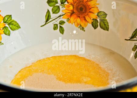 Öl, das in eine Metallschüssel in die Milch gegossen wird. Teigzubereitung. Rezeptpuffer-Gebäck. Backzutaten, Nahaufnahme, Draufsicht. Stockfoto